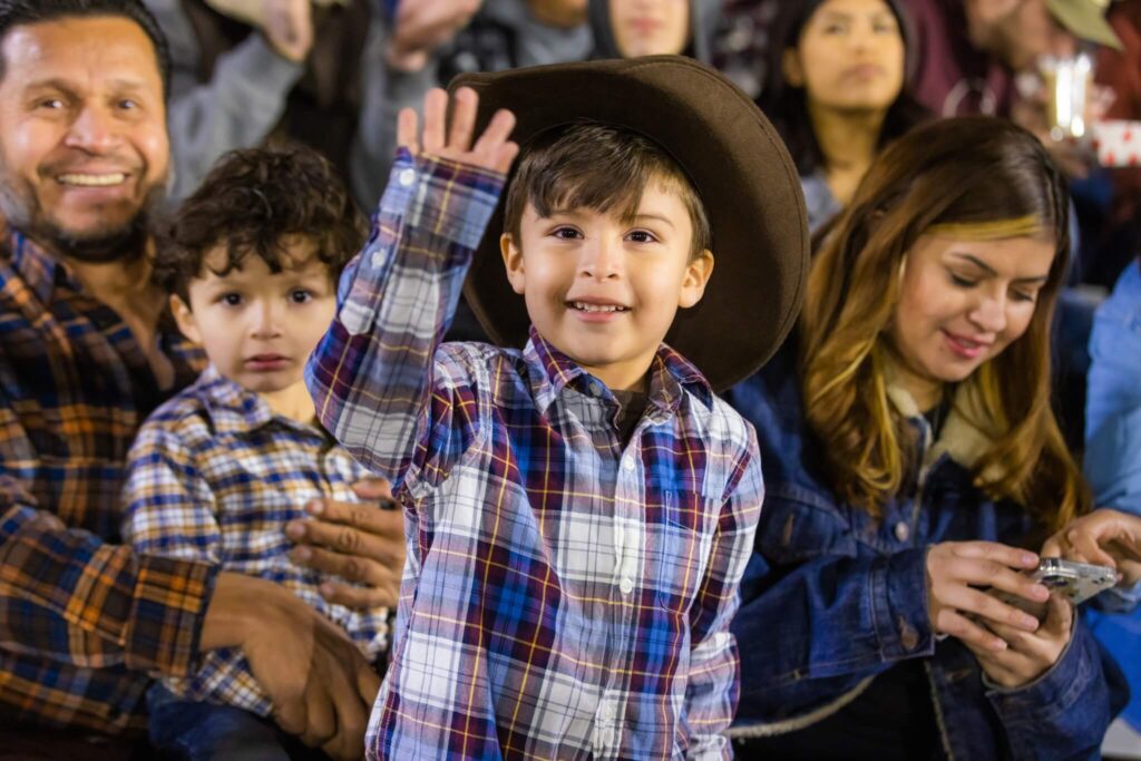young boy with cowboy hat waves at camera during las vegas rodeo