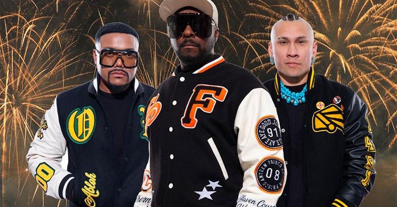 black eyed peas singers pose for camera with fireworks in the background